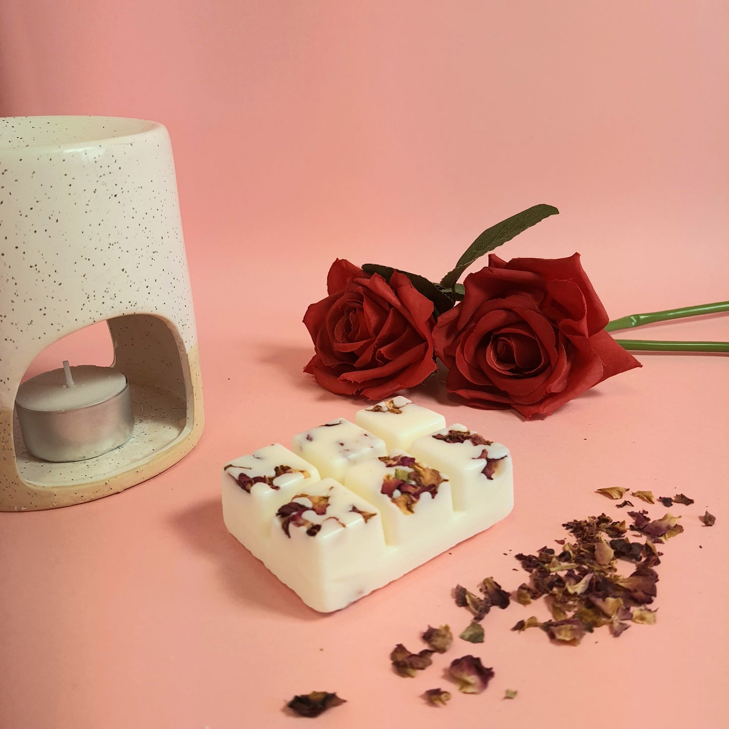 Rose & Sandalwood soy wax melts adorned with dried rose petals, a sensual spring scene with a light pink background, and wax melts surrounded by beautiful rose petals. A wax melt burner set to the side to give off warm cozy vibes.