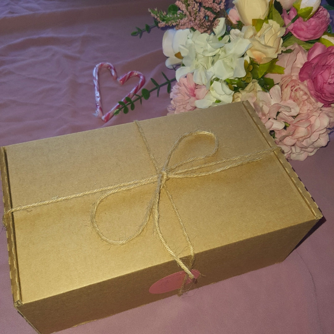 Brown gift box with string bow on a pink surface with flowers and candy canes