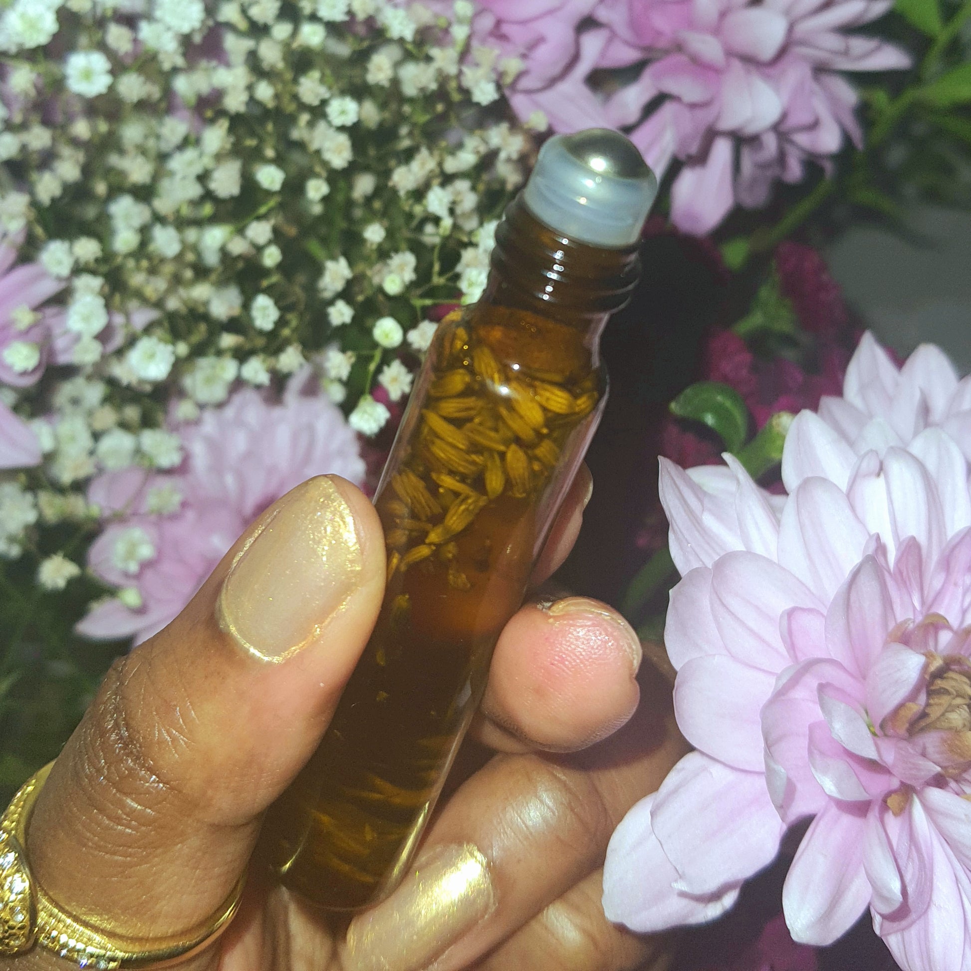 Hand holding a small brown essential oil roller bottle with flowers in the background