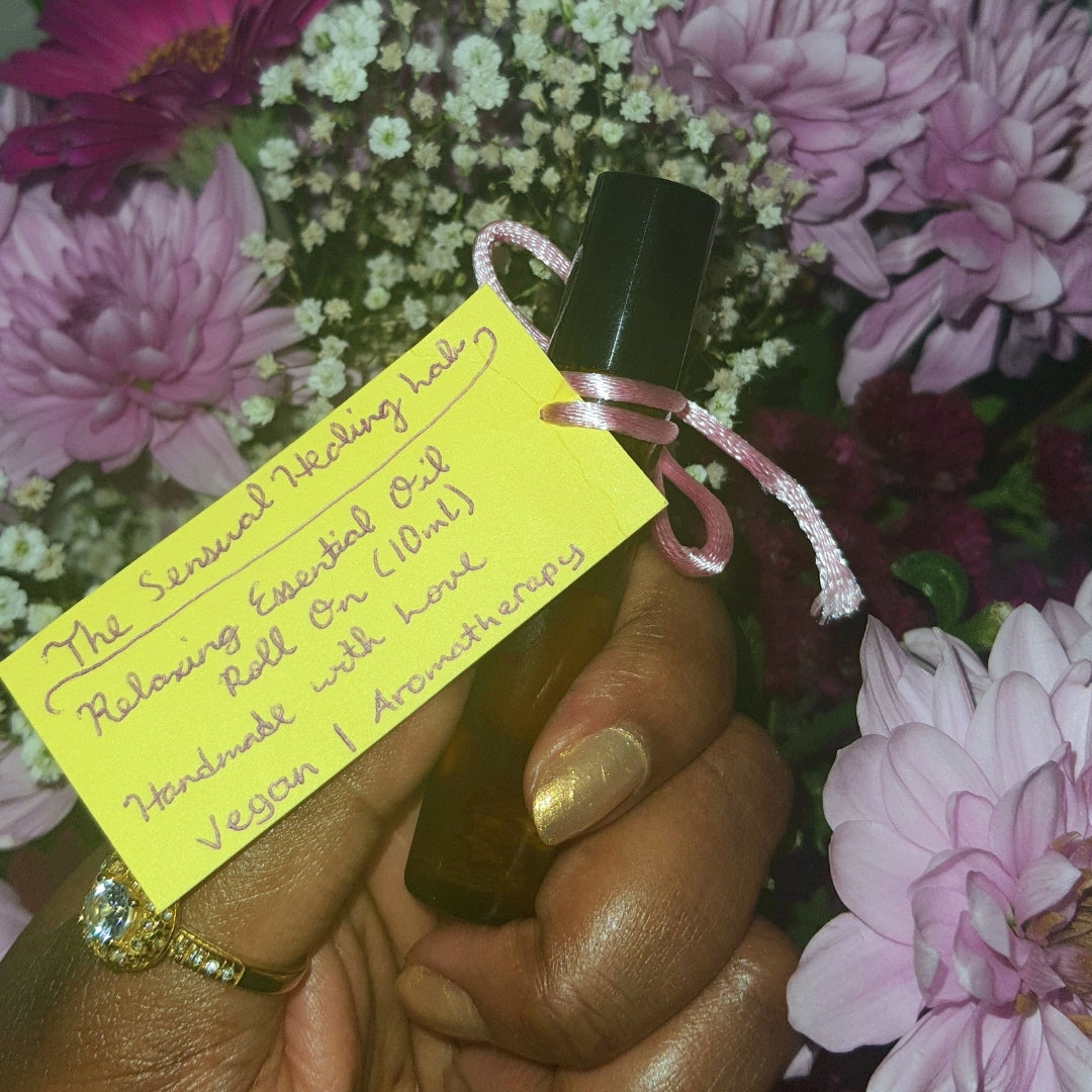 Hand holding a bottle of essential oil roll on with the sensual healing lab yellow tag against a floral background