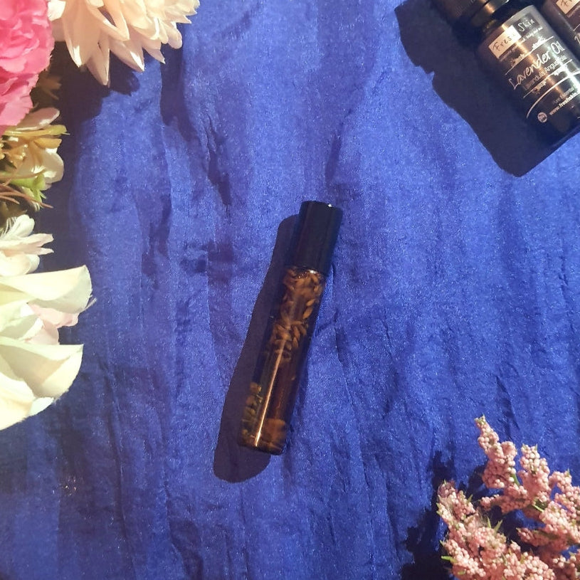 Essential oil roll on bottle, with lavender and ylang ylang essential oil bottles on a blue fabric background with flowers. Giving off sensual vibes