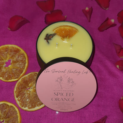 Spiced orange soy wax candle, against sultry pink background, surrounded by dried orange slices and rose petals, creating a romantic vibe