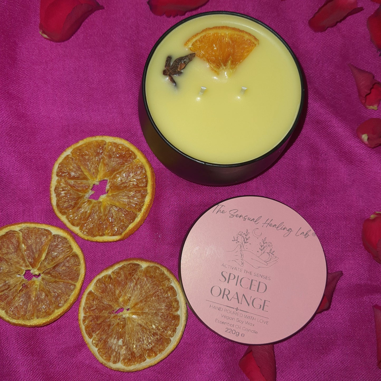 Spiced orange soy wax candle, against sultry pink background, surrounded by dried orange slices and rose petals, creating a romantic vibe